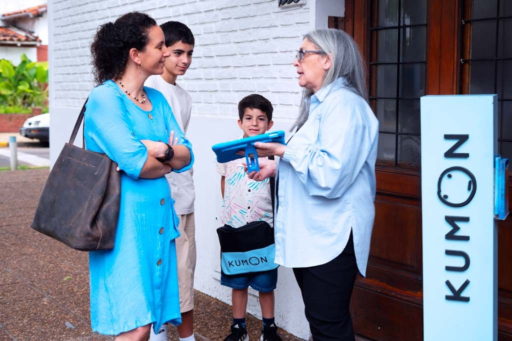 Frente a la fachada de una nueva franquicia Kumon, la orientadora con una mujer y dos niños
