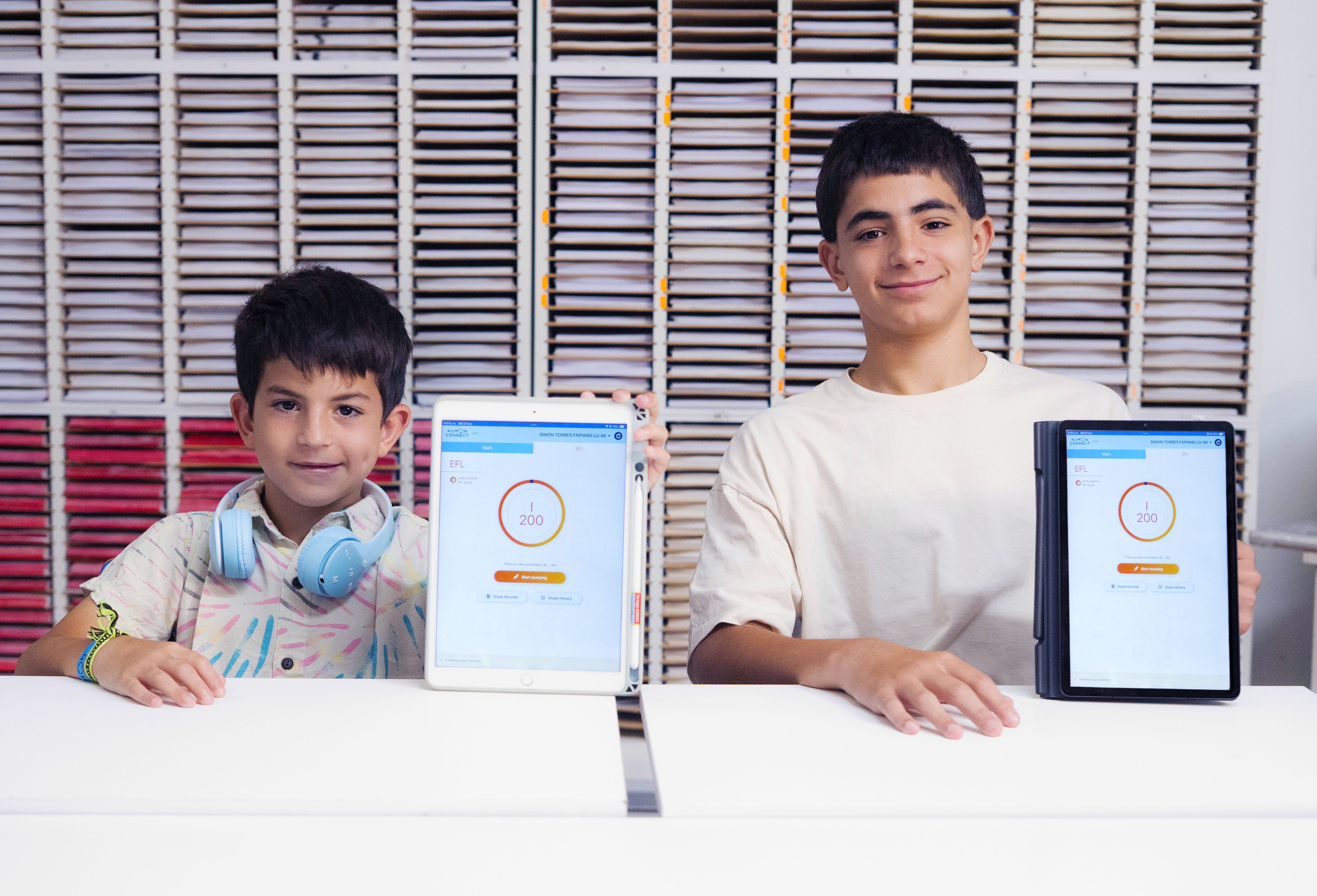 Dos estudiantes mostrando sus avances en tabletas mientras aplican el método Kumon de estudio individualizado.